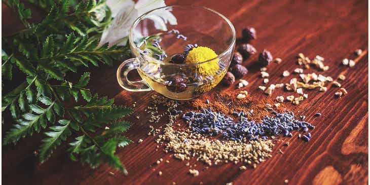 Przezroczysta filiżanka z herbatą ziołową i kwiatami przyrządzona według receptur medycyny holistycznej, postawiona na stole.
