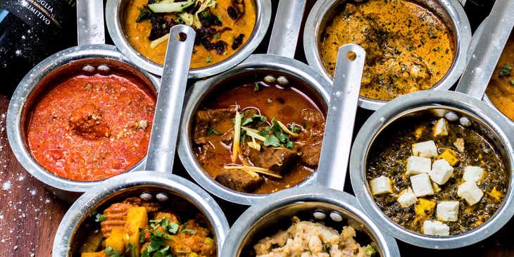 Srebrne, miniaturowe garnuszki wypełnione różnymi daniami serwowanymi w restauracji indyjskiej.