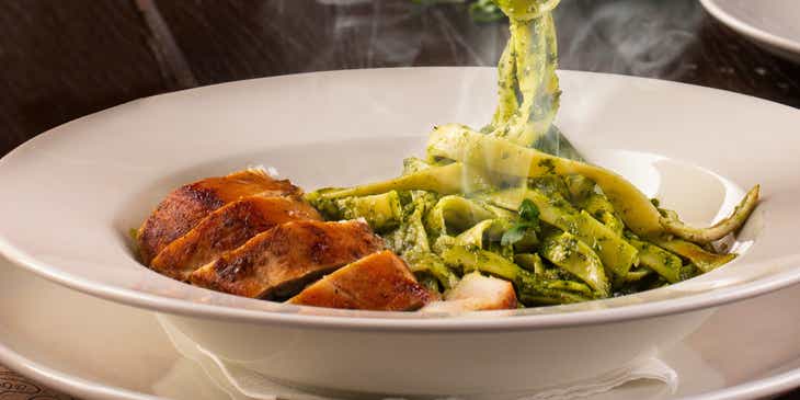 Pasta z zielonym pesto i plastrami kurczaka podawana w restauracji włoskiej.