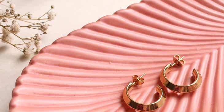 Gouden oorbellen op een geribbeld, roze schaaltje.