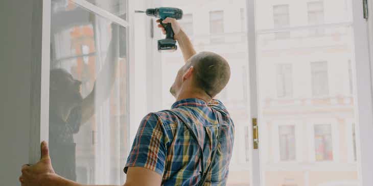 Un handyman que trabaja para una empresa de mantenimiento de propiedades instalando una ventana en un apartamento, en un logo para mantenimiento de propiedades.