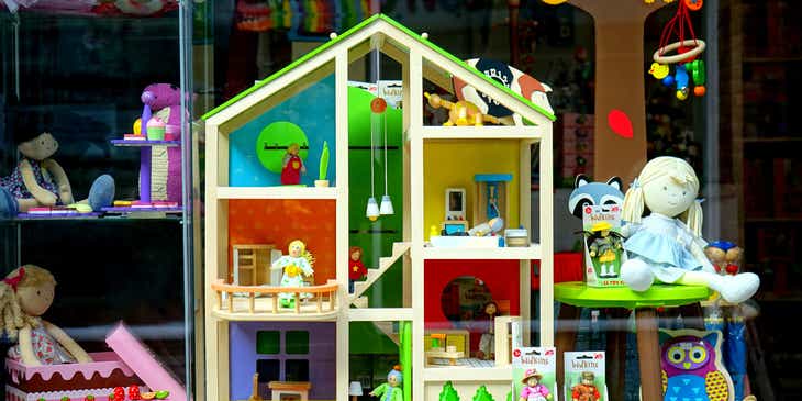 Domek dla lalek i maskotki zaprezentowane w witrynie sklepu z zabawkami.