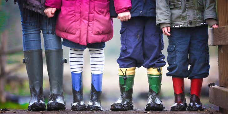 Un gruppo di bambini che indossano dei vestiti e degli stivali da pioggia colorati ricoperti di fango.