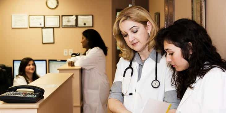 Krankenschwestern schauen während ihrer Schicht in einer Klinik in eine Patientenakte und tauschen sich untereinander aus.