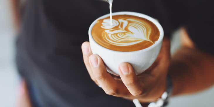 Un hombre vertiendo leche espumosa en una taza de café recién hecho en un logo de café