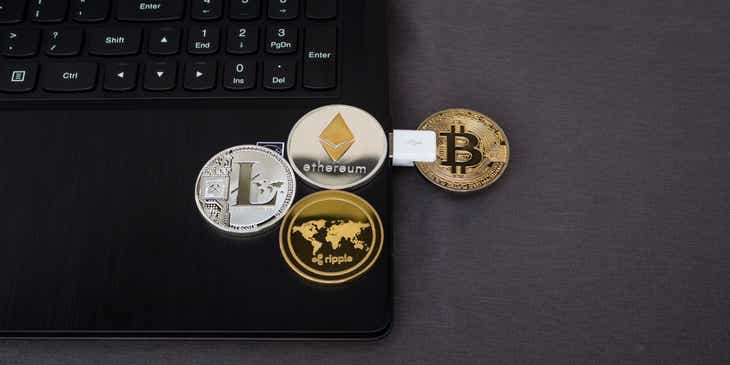 Monety przedstawiające różne kryptowaluty ułożone na stole i laptopie.