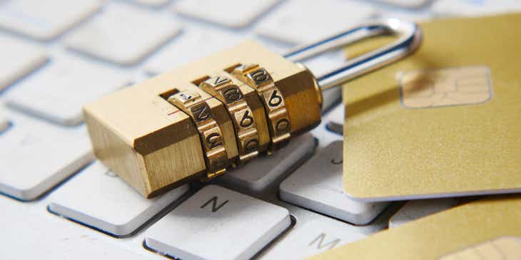 Ein Nummernschloss auf einer Tastatur neben zwei goldenen Kreditkarten als Symbol für IT-Sicherheit.