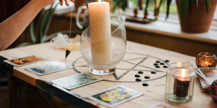 Una vela encendida sobre una mesa rodeada de cartas de tarot y objetos esotéricos.