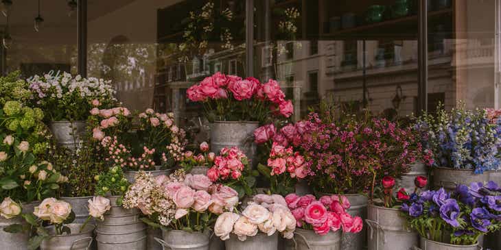 An assortment of tall buckets containing pink and blue flowers outside a florist.