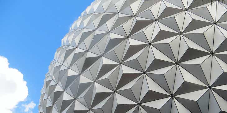Una vista exterior de un edificio que presenta elementos de diseño geométrico con una franja de cielo azul visible en el fondo en un logo geométrico.