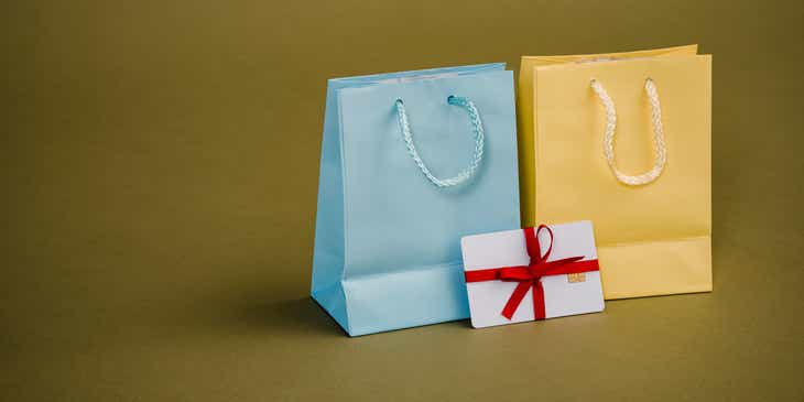 Um cartão-presente cuidadosamente embrulhado ao lado de duas sacolas de presentes.