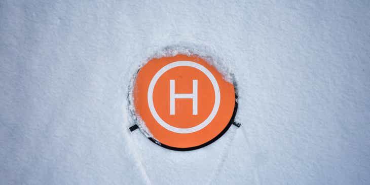 Biała litera „H” na pomarańczowej powierzchni otoczonej śniegiem.