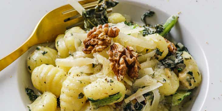 Un piatto di gnocchi con noci, formaggio e cime di rapa, sul tavolo di un ristorante italiano.