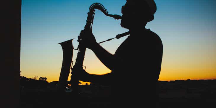 Siluet seorang pria memainkan musik jazz dengan saksofon saat matahari terbenam.