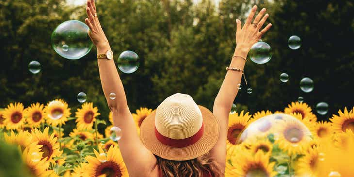 Bir ayçiçeği tarlasında yürüyen kollarını kaldırmış sevinçli bir kadın.