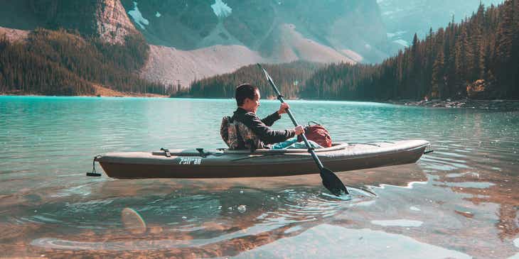 Een persoon in een kajak op een meer en tegen een berglandschap als achtergrond.