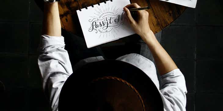 Pessoa sentada em uma mesa desenhando um design de logotipo.