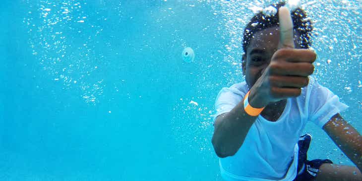 Seorang anak laki-laki menunjukkan jempol di bawah air saat belajar berenang di les renang.