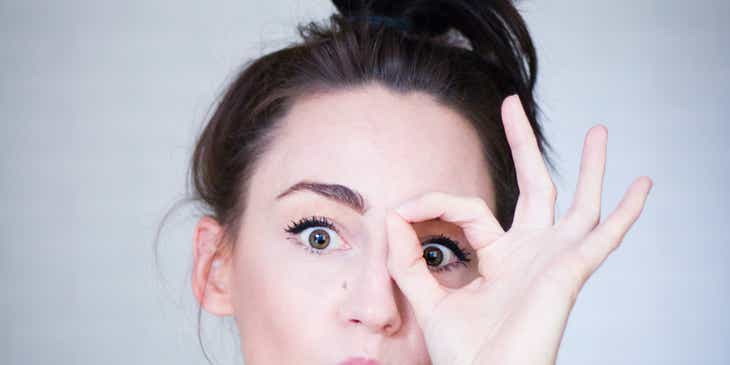 Uma mulher fazendo uma careta engraçada e destacando um dos olhos com a mão.