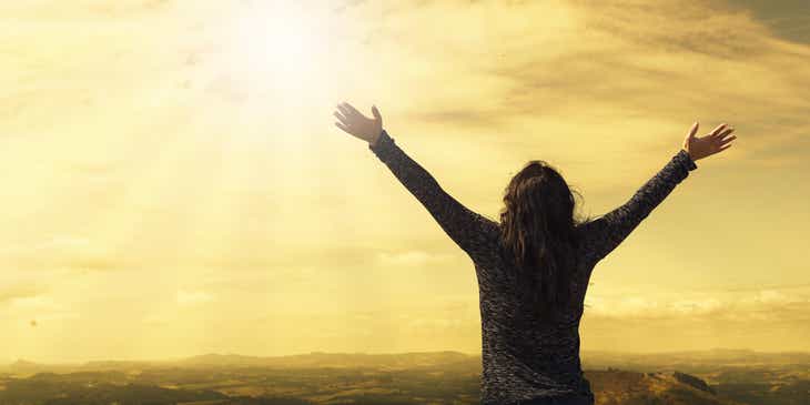 Une femme religieuse avec les bras ouverts vers les cieux et le soleil.