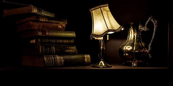 Een stapeltje oude boeken, een schemerlampje en een zilveren koffiepot weerrgegevern in een visueel donkere stijl.