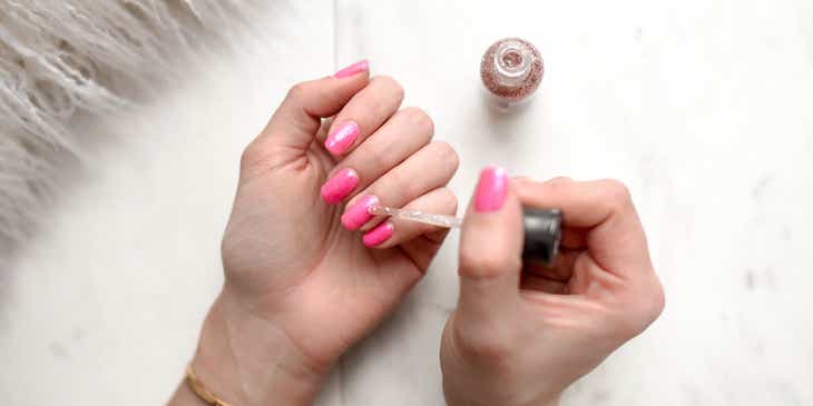 Seseorang sedang memakai nail polish berwarna pink.