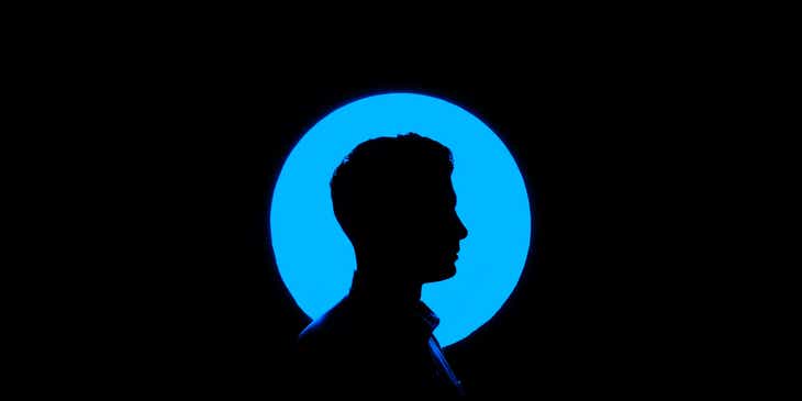 Profil mężczyzny tworzący negatywną przestrzeń na tle niebieskiego, okrągłego neonu.