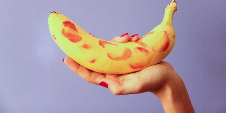 Een ondeugende foto van een hand die een banaan vol met lippenstiftafdrukken vasthoudt.