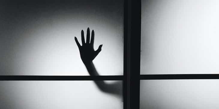 Una mano inquietante di una creatura paranormale che preme contro una finestra.