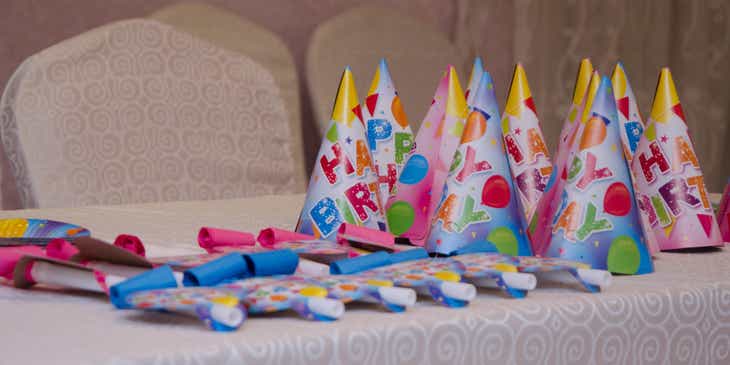 Czapeczki i trąbki urodzinowe ułożone na stole z artykułami imprezowymi.