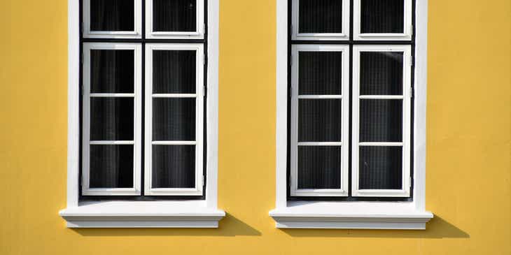 Dua jendela berbingkai putih di sebuah dinding berwarna kuning.