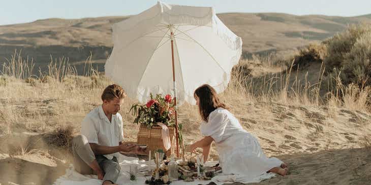 A couple enjoying a romantic picnic on a sandy beach.