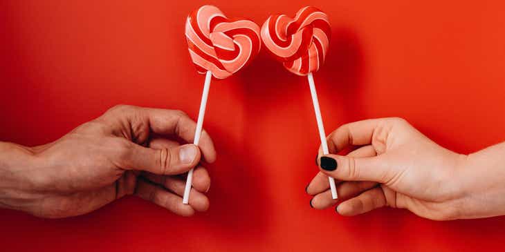 Two people holding romantic heart-shaped lollipops.