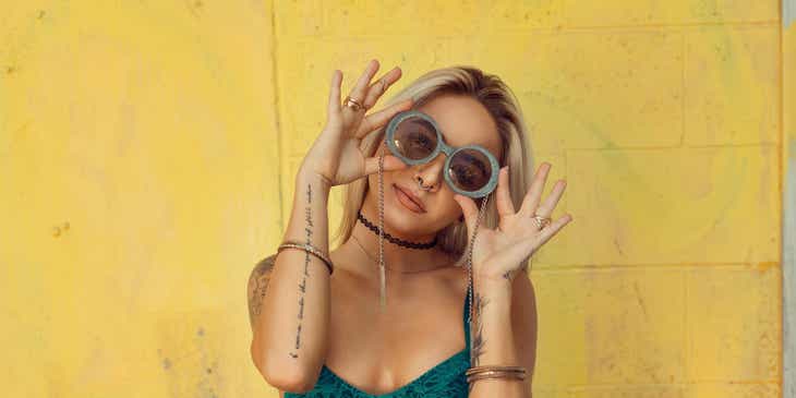 Una donna tatuata che indossa un crop top irriverente e gioca con i suoi occhiali da sole.