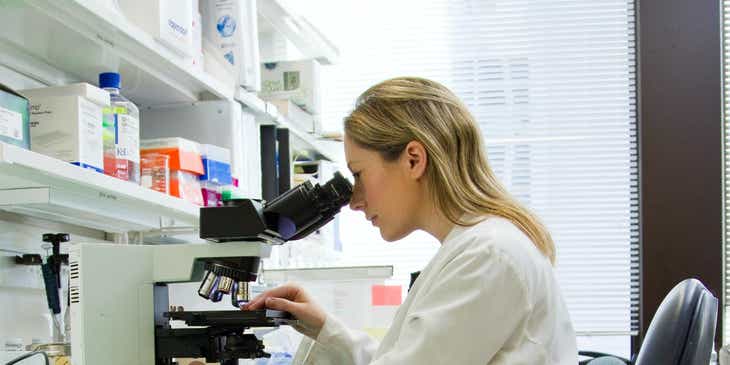 Seorang ilmuwan sedang menyelidiki spesimen menggunakan mikroskop di sebuah laboratorium sains.