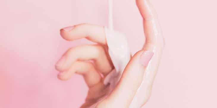 Hautmilch wird vor einem pinken Hintergrund auf eine Hand gegossen.