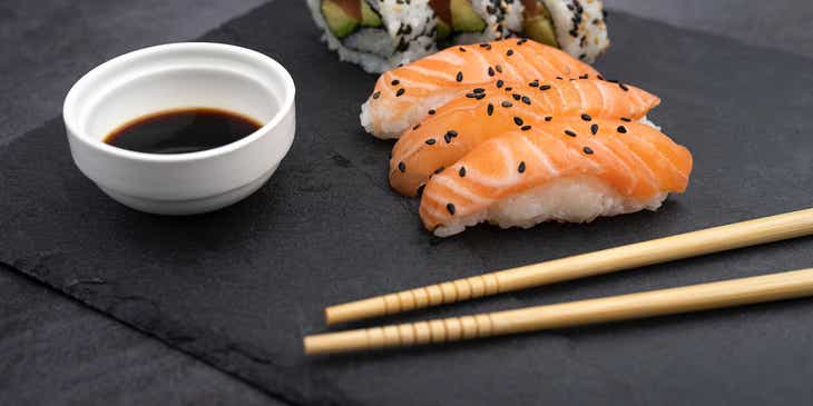 Sepiring sushi dengan sumpit dan kecap.