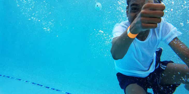 Un bambino che mostra il pollice mentre è sott'acqua per indicare che è tutto okay mentre sta facendo una lezione in piscina in una scuola di nuoto.