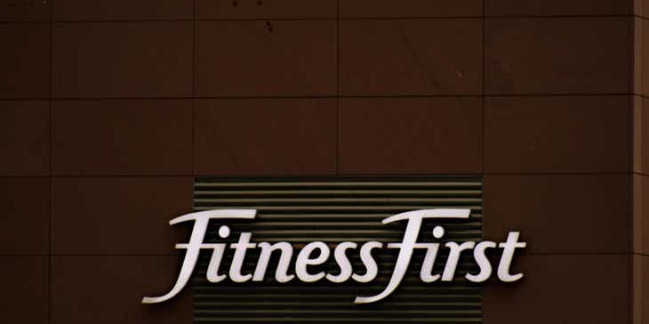 Ein weißes Textlogo der Firma Fitness First auf einem dunklen Hintergrund.