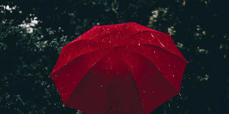 Seseorang memegang payung merah di tengah hujan.
