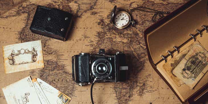 Vintage items, waaronder een ouderwetse fotocamera, horloge, notitieboekje en enkele ansichtkaarten, uitgestald op een antiek ogende wereldkaart.