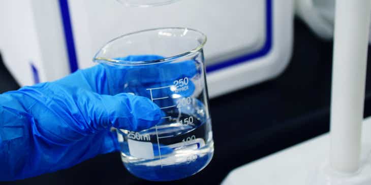 Eine Person mit einem blauen Handschuh hält in einem Labor ein Glas mit aufbereitetem Wasser, um dessen Qualität zu analysieren.