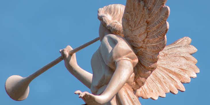 Escultura de un ángel con alas y una trompeta con un cielo azul de fondo.