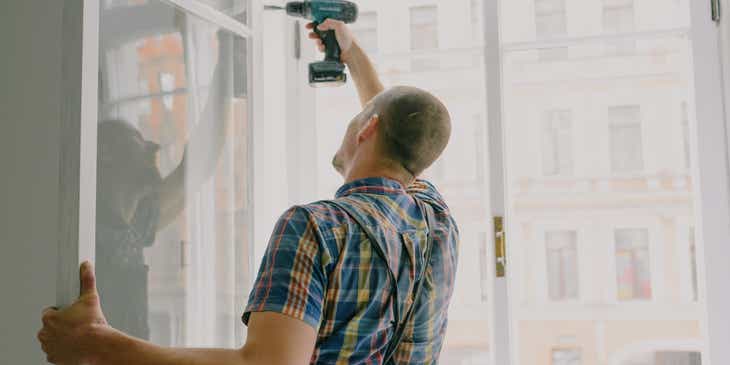 Seorang tukang yang bekerja untuk bisnis pemeliharaan properti memasang jendela di sebuah apartemen.