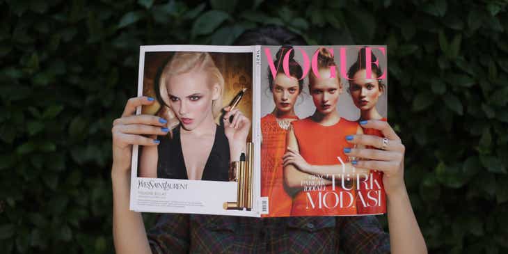 Eine Frau hält sich das geöffnete Modemagazin Vogue vors Gesicht.