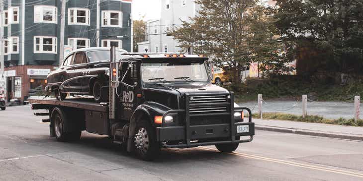 A black tow truck driving down a road.