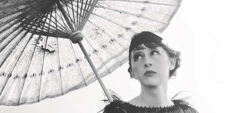 Een vrouw met jaren 20 stijl zittend onder een parasol.