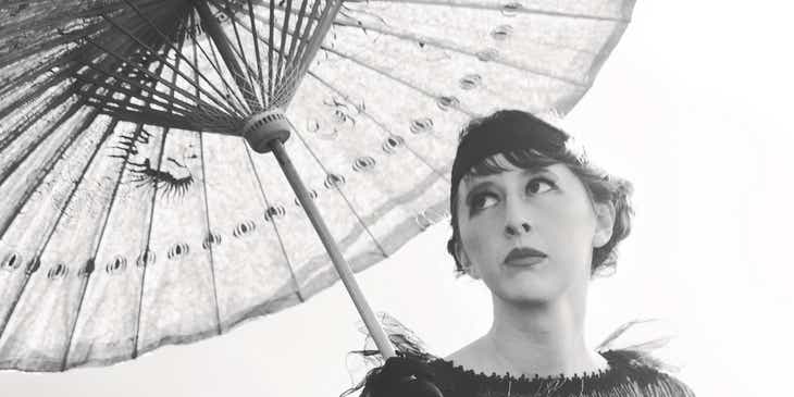 Seorang wanita dari tahun 1920an yang sedang duduk di bawah payung.