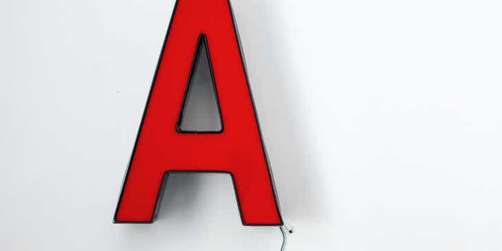 Una lampada a forma di lettera "A" rossa, spenta e appesa al muro.