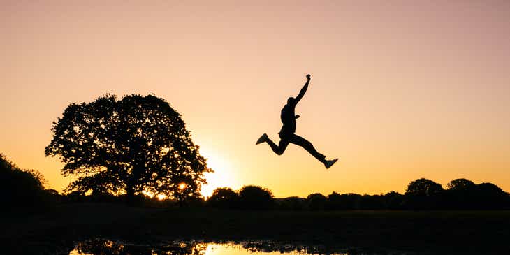 An action photo of a silhouetted person leaping over a lake.